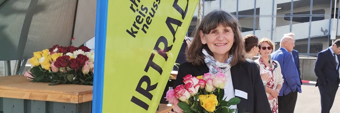 Eine Frau mit einem Blumenstrauß in der Hand. Die Frau steht vor einem Schild mit der Aufschrift "Fairtrade".