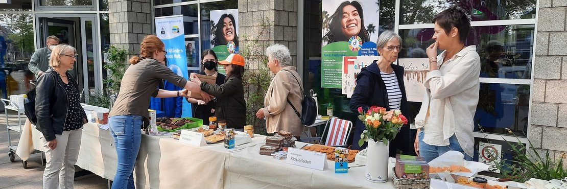 Eine lange Tafel mit fairen Produkten vor der ein paar Menschen stehen