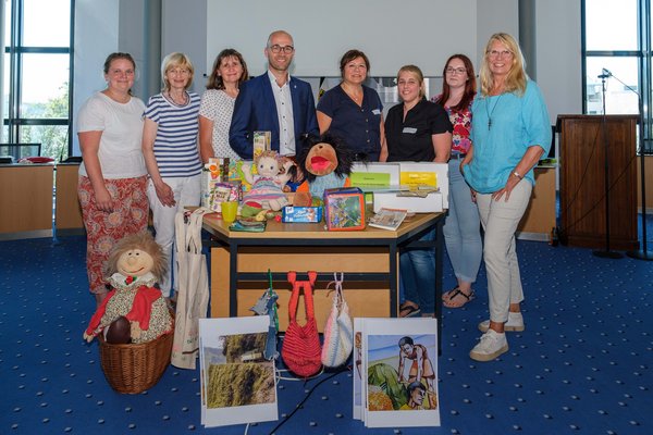 Gruppenfoto: Menschen hinter Tisch mit fairen Produkten, Handpuppen und Informationsmaterial