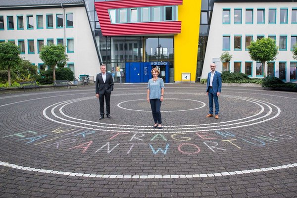 Landrat Hans-Jürgen Petrauschke, Benjamin Josephs und Renate Kuglin stehen vor dem Kreishaus in Grevenbroich. Auf dem Boden vor Ihnen steht mit Kreide "Wir tragen Fairantwortung" geschrieben. 