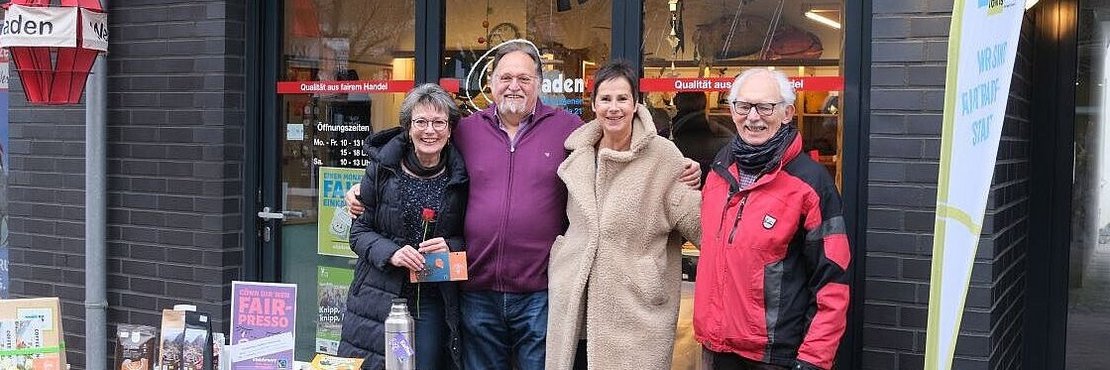 Zwei Frauen und zwei Männer stehen hinter einem Tisch. Auf dem Tisch werden faire Produkte präsentiert.