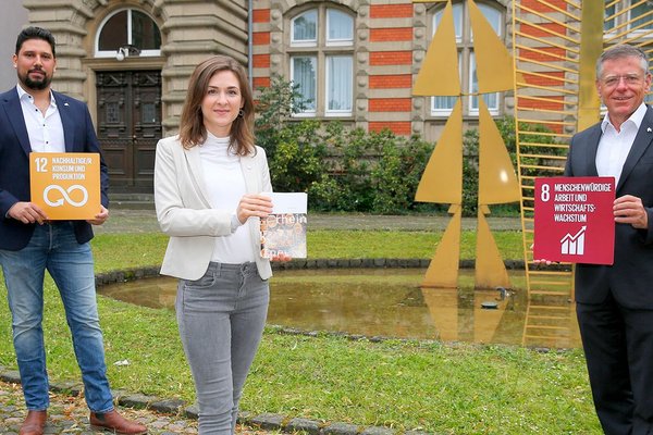 Thiago de Carvalho Zakrzewski mit Schild: "12 Nachhaltige/r Konsum und Produktion"; Verena Tranzer mit Broschüre und Hans-Jürgen Petrauschke mit Schild "8 Menschenwürdige Arbeit und Wirtschaftswachstum"