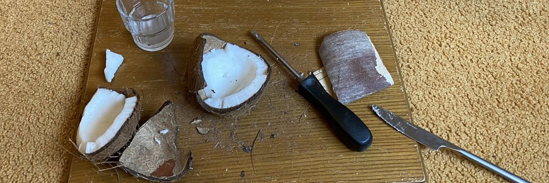 Ein Ausschnitt von Kokosnussschalen, mit verschiedenen Werkzeugen wie einem Hammer, Raspel, Schleifpapier und einem Messer, sowie einer kleinen Anleitung und einer Packung Kokoschips.