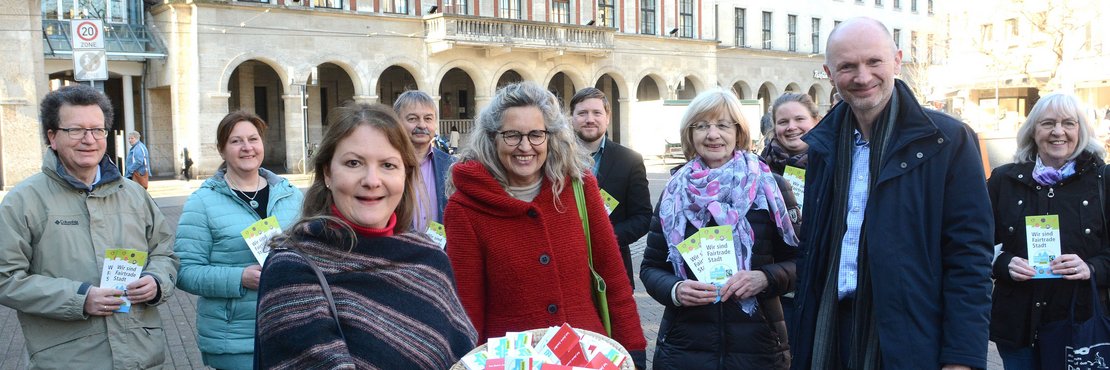 Personen stehen auf einem Marktplatz und halten einen Korb mit fairer Schokolade und Flyer hoch