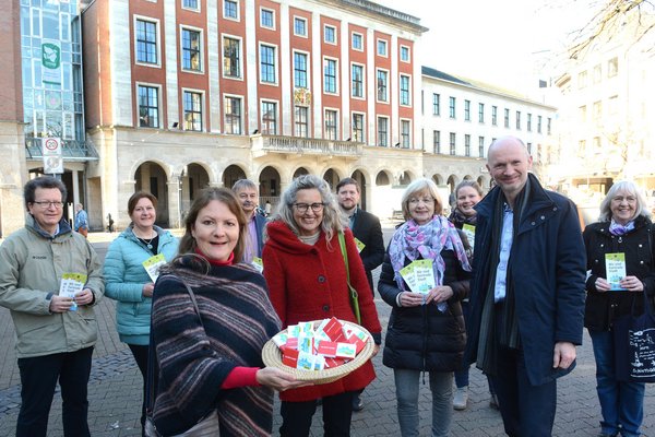 Personen stehen auf einem Marktplatz und halten einen Korb mit fairer Schokolade und Flyer hoch