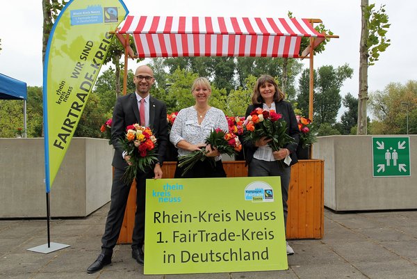Kreis-Pressesprecher Benjamin Josephs, Melanie Schröder und Petra Koch vor einem Stand mit fairen Rosen
