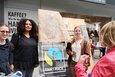 Drei Frauen stehen neben einem Plakat von "Fairtrade" an einem Marktstand.