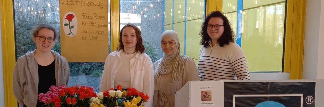 Vier junge Frauen hinter einem Tisch, auf dem Rosen stehen.